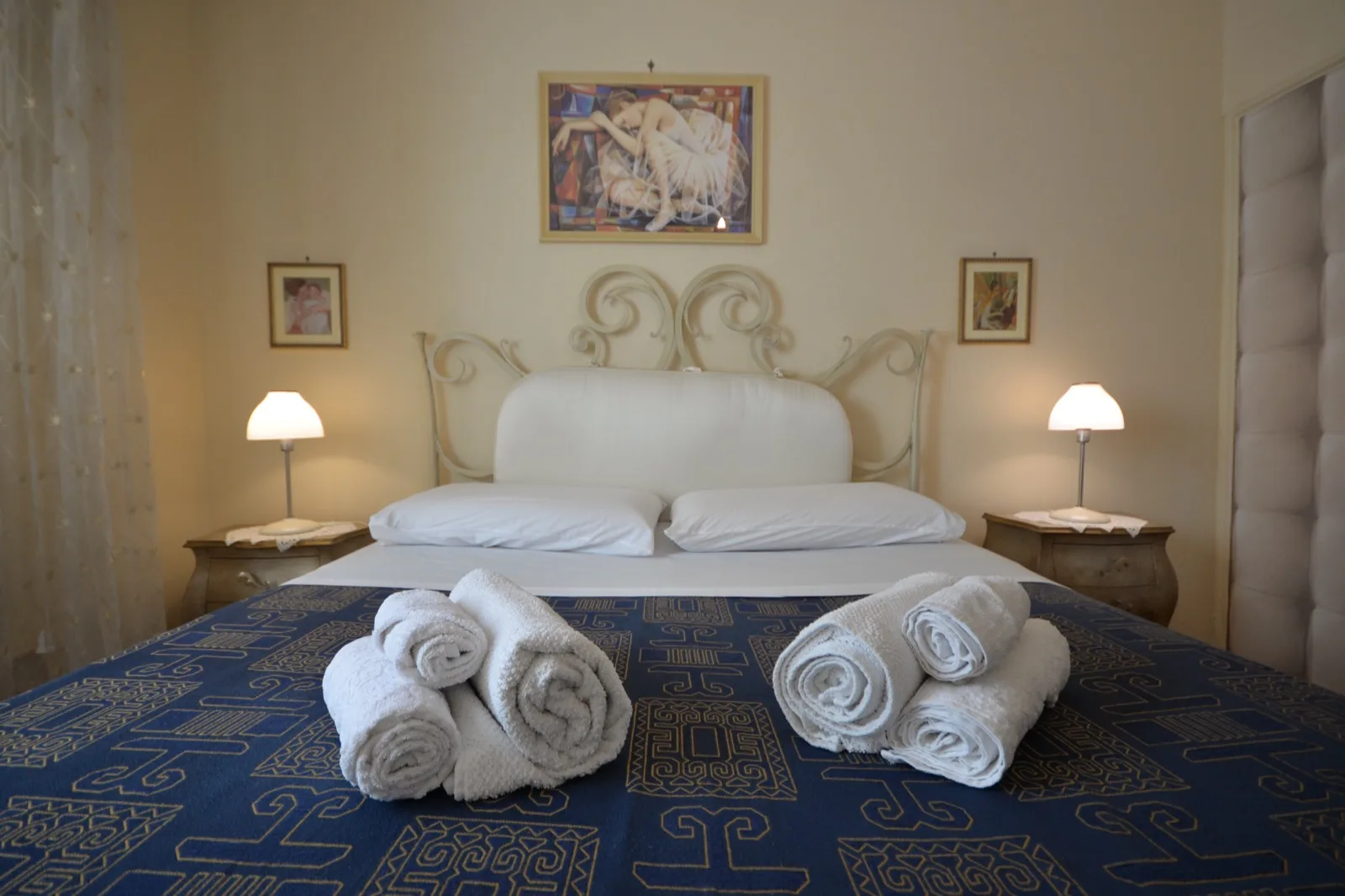 Camera matrimoniale con letto in ferro battuto color crema, copriletto blu e asciugamani puliti arrotolati